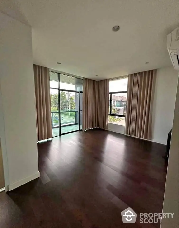 Spacious empty room with large windows and dark wood flooring, perfect for customization.