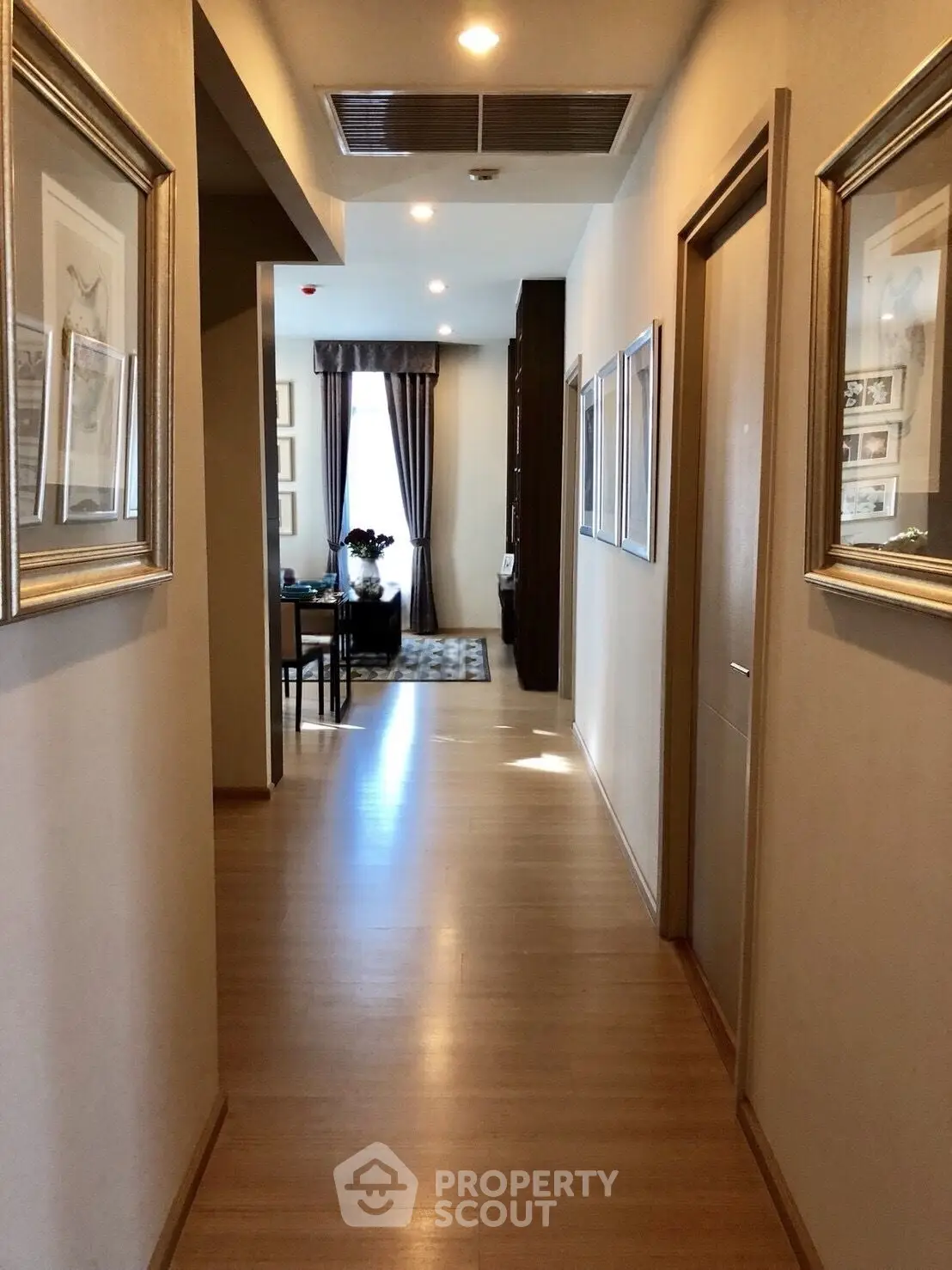 Elegant hallway leading to a stylish living area with framed art and wooden flooring.