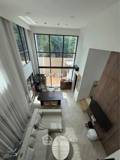 Spacious modern living room with high ceilings and large windows offering natural light and garden view.