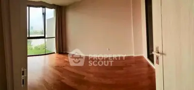 Spacious empty room with wooden flooring and large window offering natural light and scenic view.