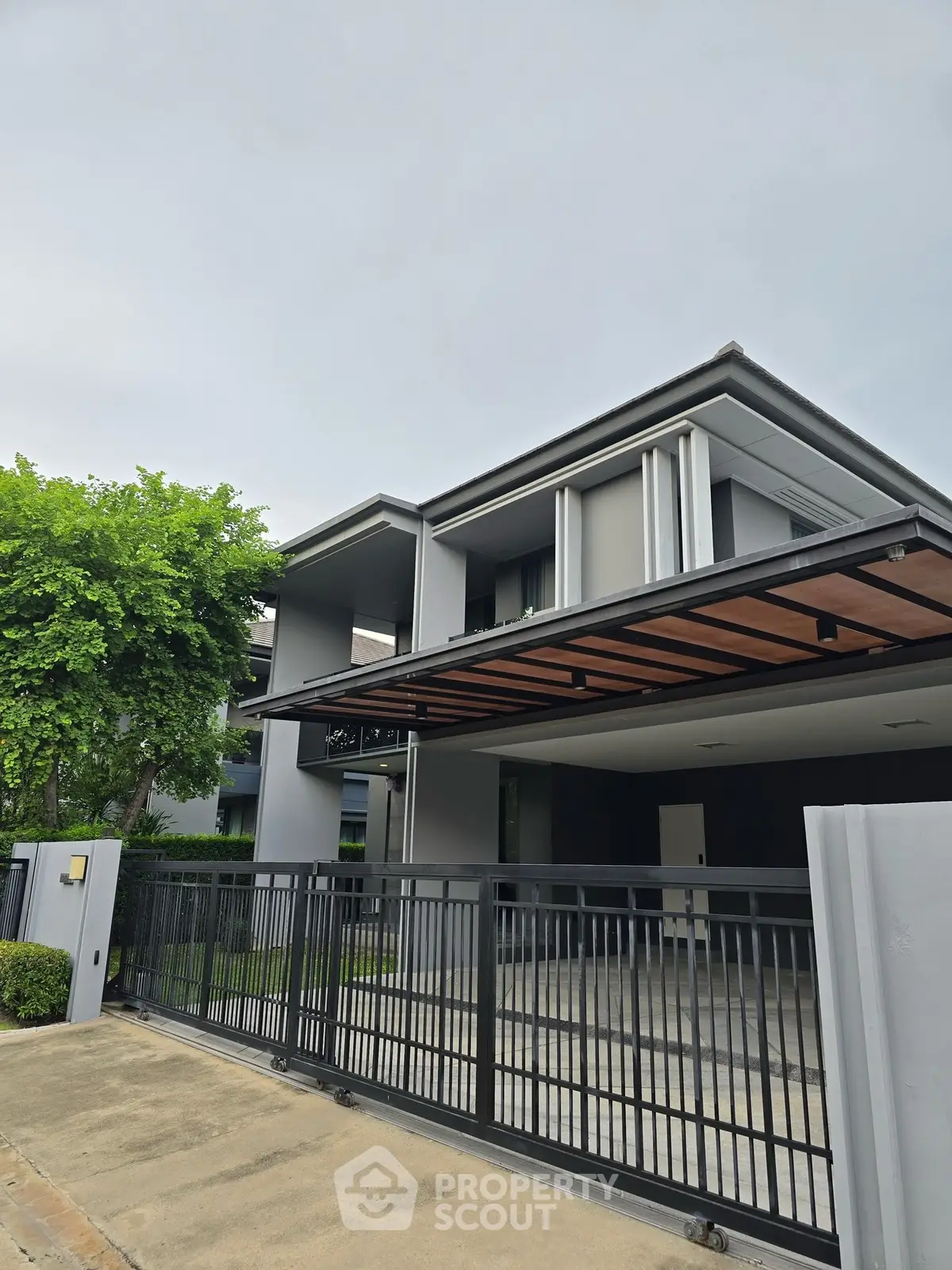 Modern two-story house with sleek design and spacious driveway, featuring a stylish gate and lush greenery.