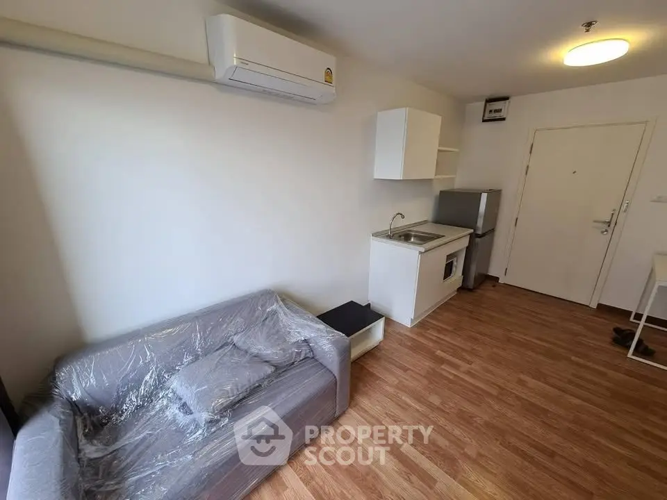 Compact studio apartment with modern kitchenette and cozy living area, featuring air conditioning and wood flooring.