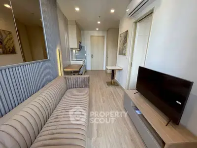 Modern living room with sleek design, featuring a plush sofa, flat-screen TV, and open kitchen layout.