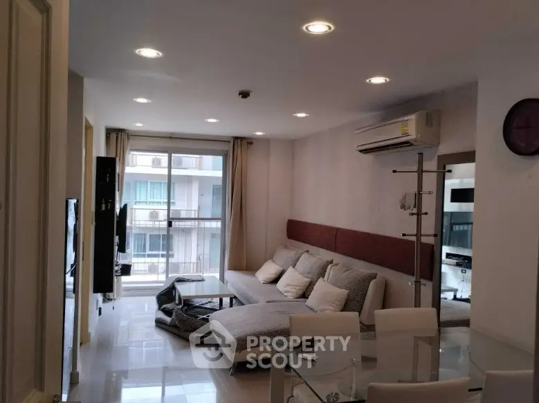 Modern living room with cozy sectional sofa and glass dining table, featuring a balcony view.