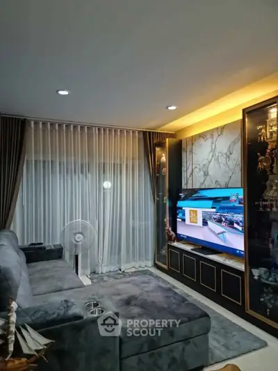Luxurious living room with plush gray sofa, large TV, and elegant decor, perfect for relaxation and entertainment.