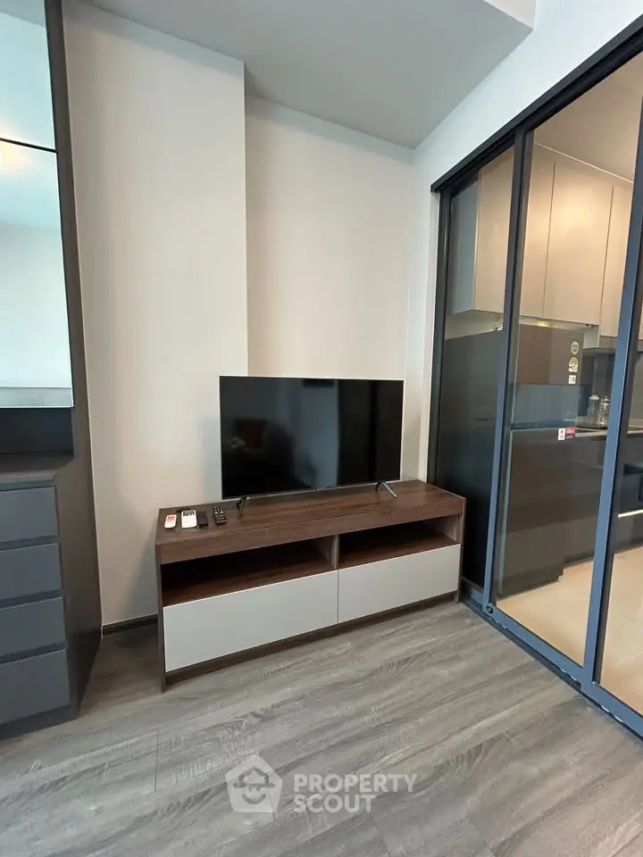 Modern living room with sleek TV stand and glass sliding doors leading to kitchen.