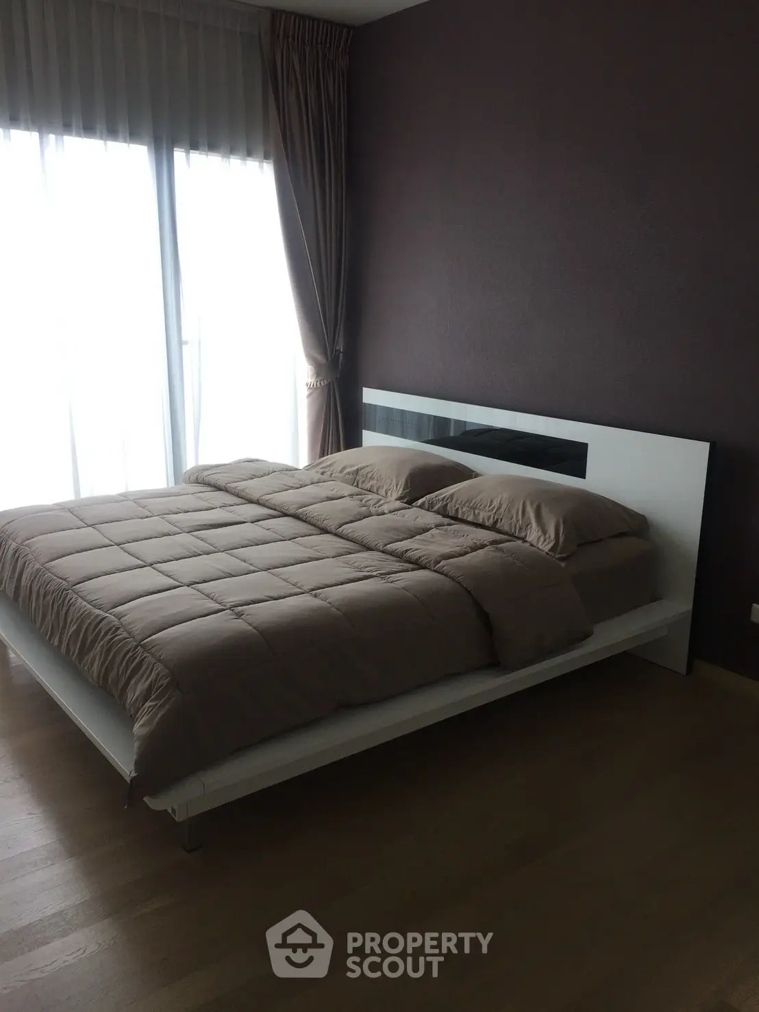 Modern bedroom with large window and elegant curtains, featuring a stylish bed and hardwood floors.