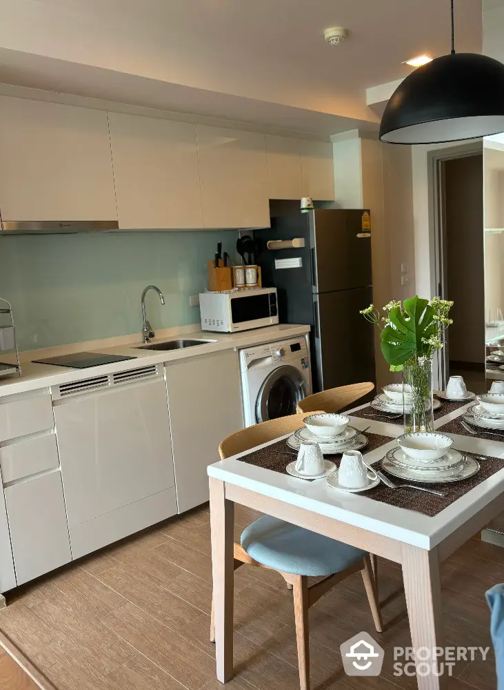 Modern kitchen with dining area, featuring sleek white cabinets and integrated appliances.