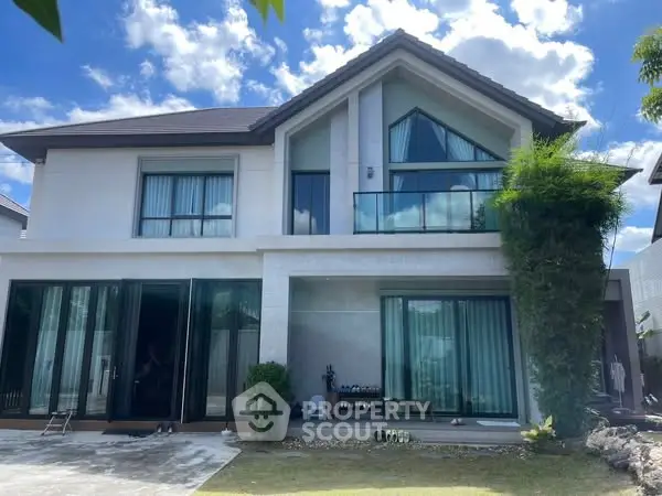 Stunning modern two-story house with large windows and lush greenery under a bright blue sky.