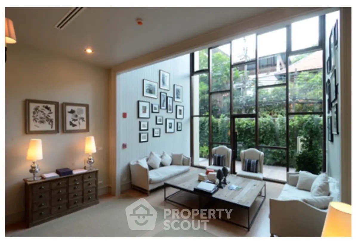 Elegant living room with large windows and garden view, featuring cozy seating and stylish decor.