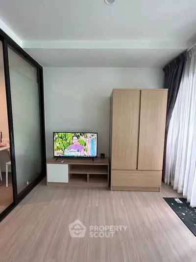 Modern living room with sleek wooden flooring, TV unit, and wardrobe, featuring large windows for natural light.