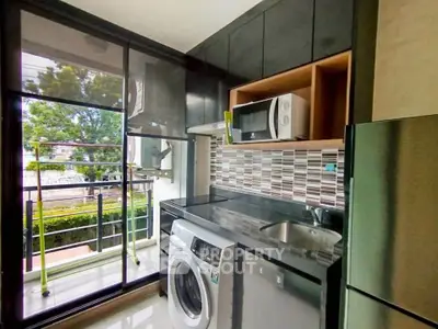 Modern kitchen with washing machine, microwave, and balcony view in stylish apartment.