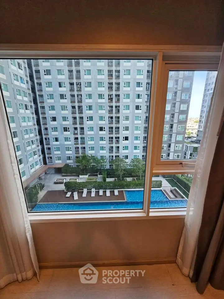 Stunning view from apartment window overlooking modern building and pool area.