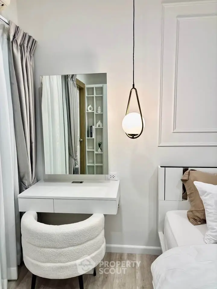 Modern bedroom with elegant vanity, plush chair, and stylish pendant light.