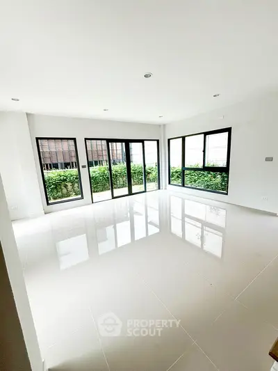 Spacious modern living room with large windows and glossy tiled floor, offering abundant natural light and garden view.
