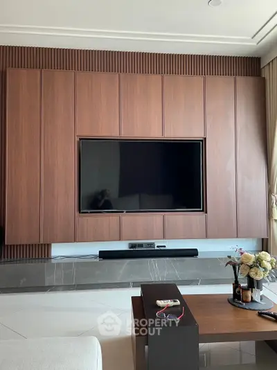 Modern living room with sleek wooden paneling and mounted TV, elegant decor and natural light.