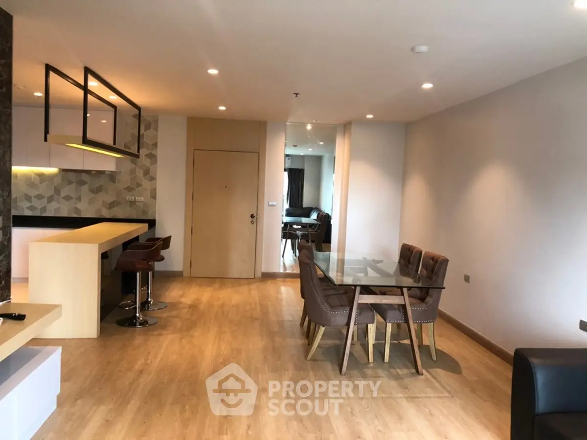 Spacious modern living room with open kitchen and dining area, featuring stylish furniture and elegant lighting.