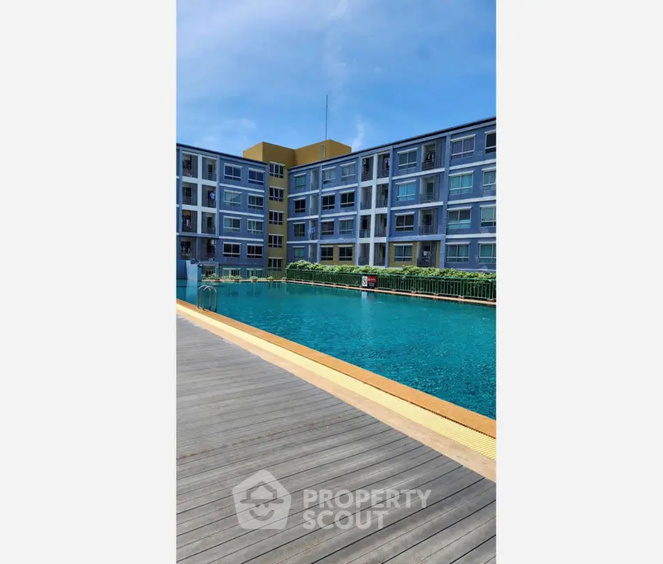 Modern apartment building with a sparkling pool and wooden deck under a clear blue sky.