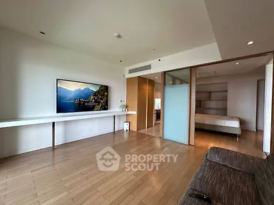 Spacious modern living room with wooden flooring and large TV, adjacent to a cozy bedroom.
