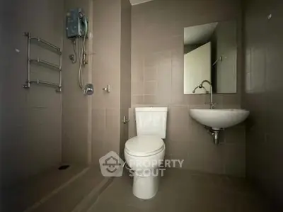 Modern bathroom with sleek fixtures and neutral tiles, featuring a shower and wall-mounted sink.