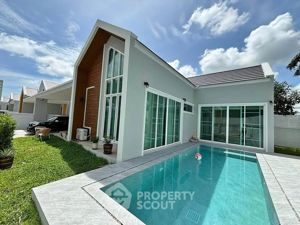 Modern single-story house with private pool and lush green lawn under a clear blue sky.