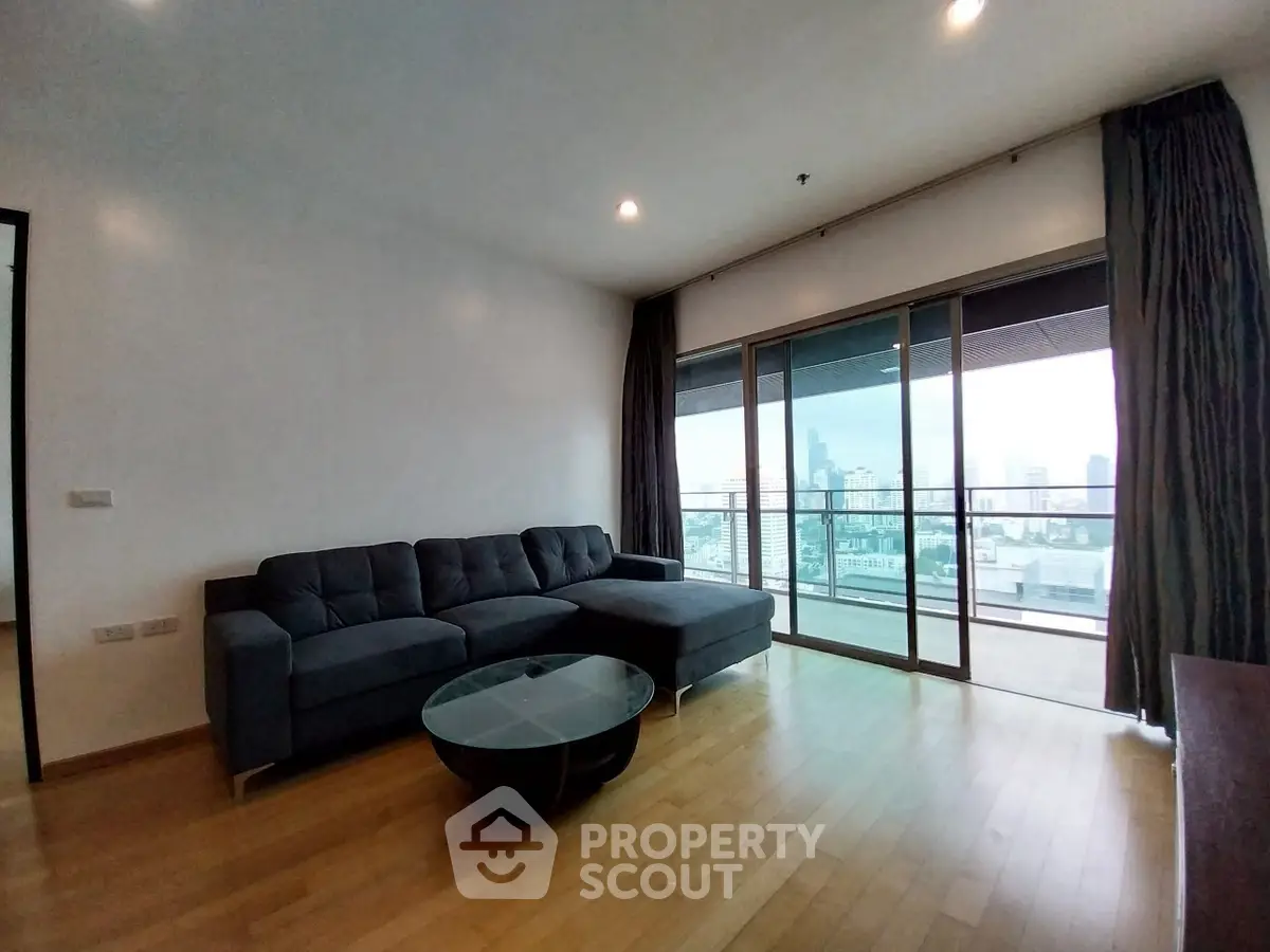 Spacious living room with modern sofa and city view balcony in high-rise apartment.