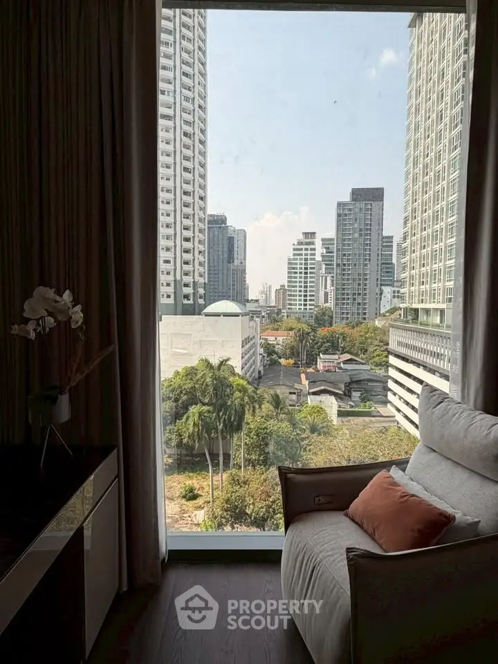 Luxurious high-rise apartment with stunning city view from large window, featuring cozy seating area.