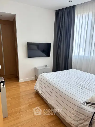 Modern bedroom with wooden flooring, striped bedding, and wall-mounted TV, featuring elegant curtains.