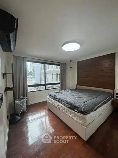 Spacious bedroom with large window and modern decor in urban apartment