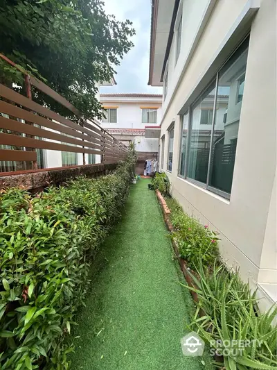 Charming garden pathway beside modern house with lush greenery and privacy fence.