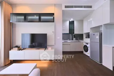 Modern open-plan living room with sleek kitchen, featuring a large TV and contemporary appliances.