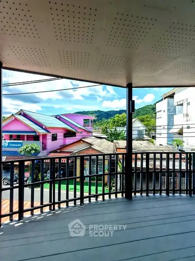 Spacious balcony with scenic view of colorful neighborhood and lush hills.