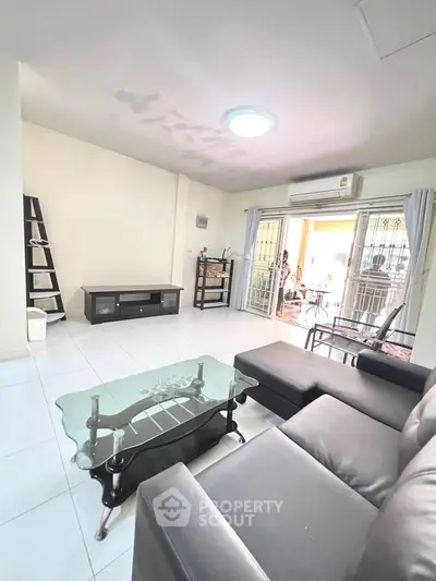 Spacious living room with modern furniture and glass coffee table, leading to a bright balcony.