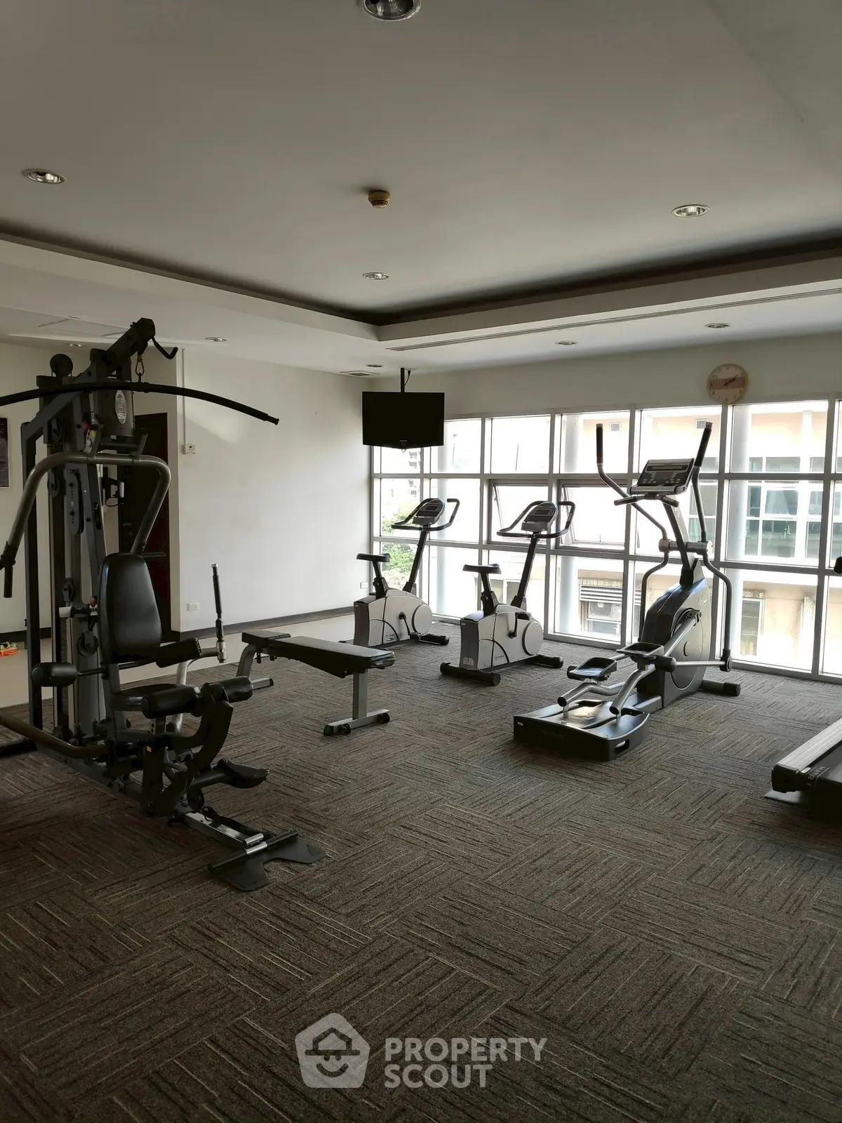 Spacious gym with modern fitness equipment and large windows for natural light.