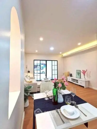 Elegant living room with modern decor and dining setup, featuring large windows and stylish lighting.