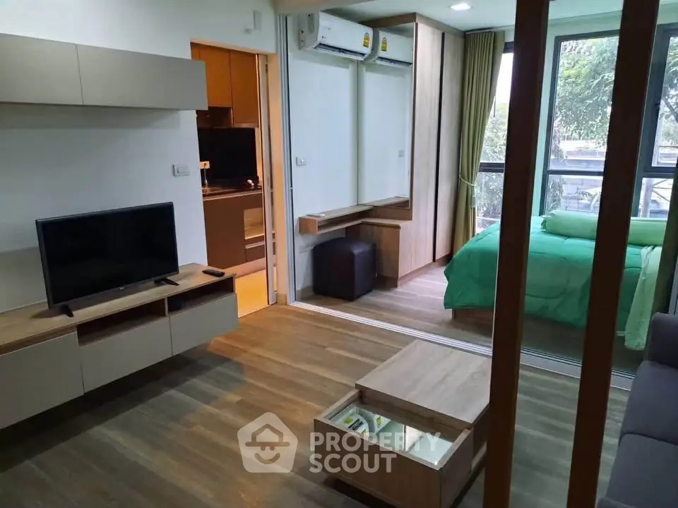 Modern apartment interior with open living room and bedroom, featuring sleek furniture and large windows.