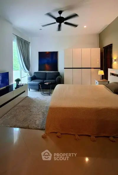 Spacious modern bedroom with cozy seating area and large window view.