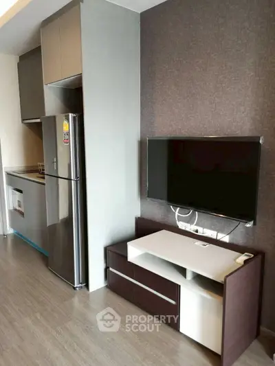 Modern kitchen with sleek cabinets and stainless steel fridge in compact apartment.