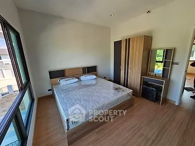 Modern bedroom with large window and wooden flooring, featuring a bed and wardrobe.