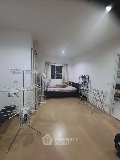 Spacious bedroom with wooden flooring and ample natural light, featuring a bed and drying racks.