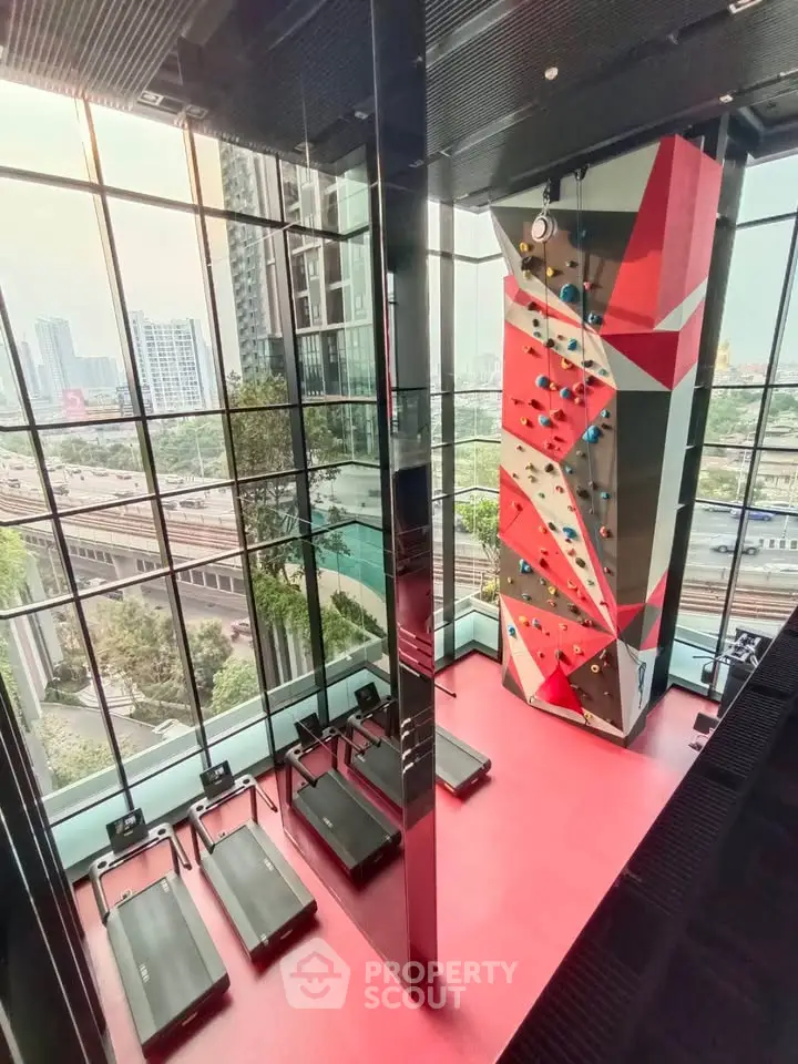 Modern gym with climbing wall and treadmills in high-rise building with city view.