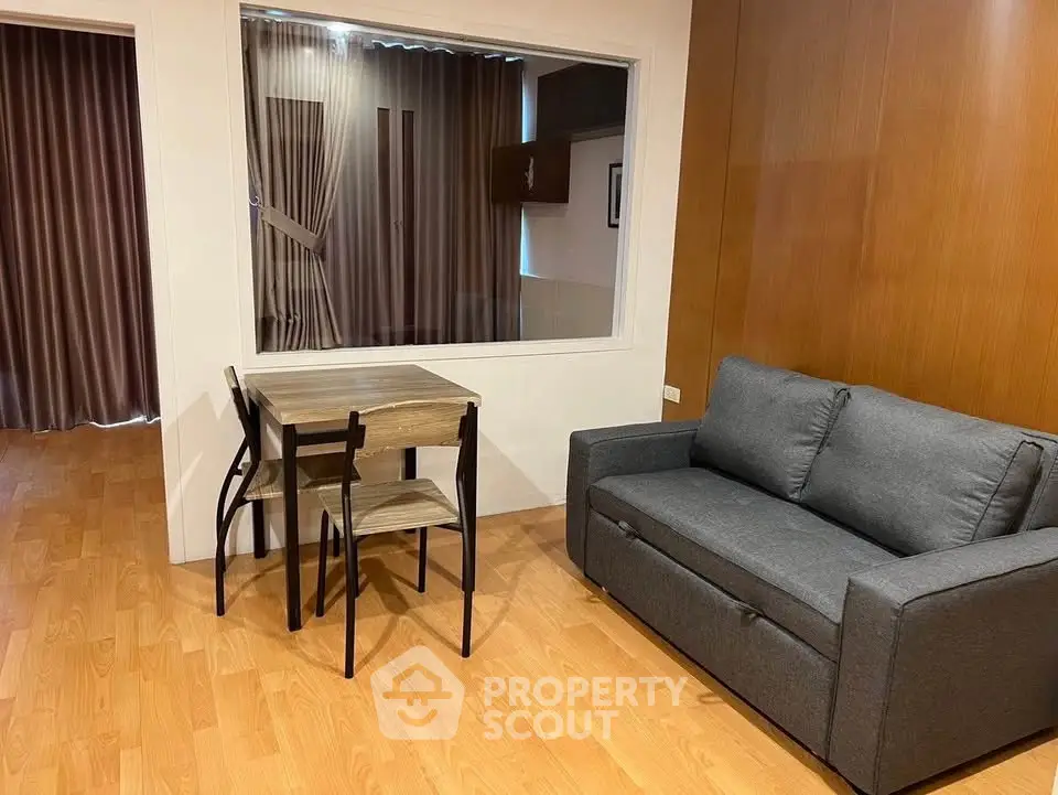Cozy living room with wooden flooring, modern gray sofa, and compact dining table set.