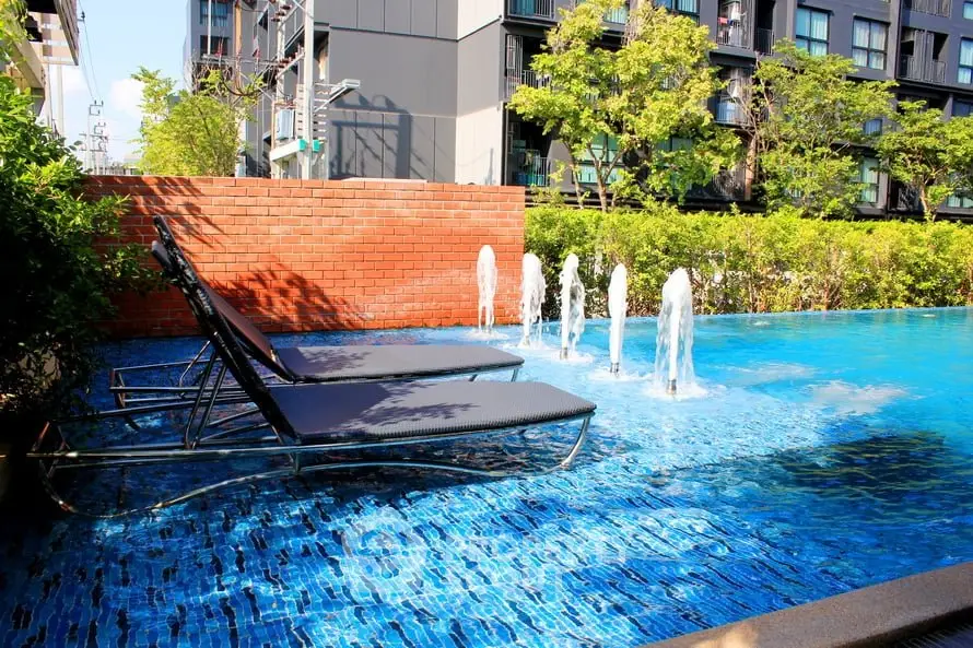 Luxurious outdoor pool area with sun loungers and water fountains in modern residential complex.
