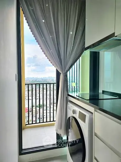 Modern kitchen with washing machine and balcony view in high-rise apartment.