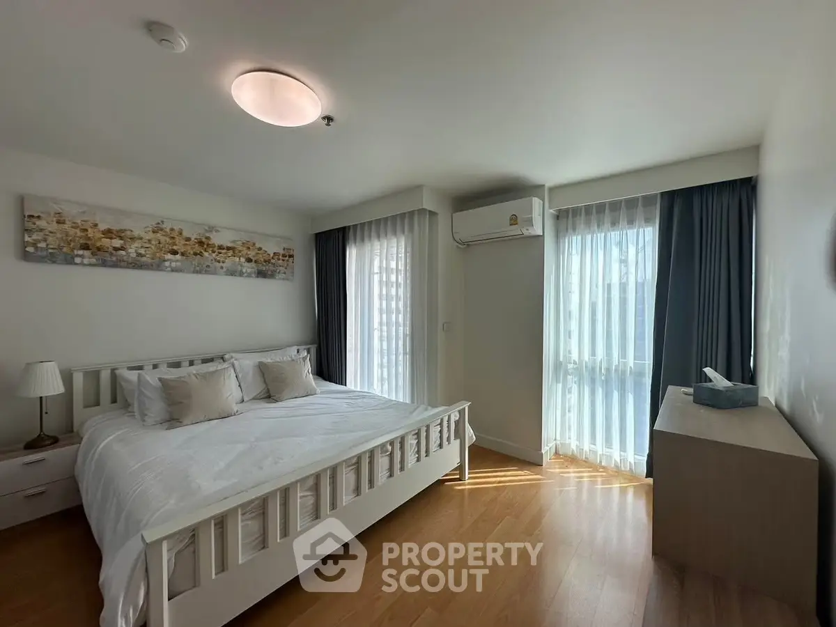 Spacious bedroom with natural light, modern decor, and wooden flooring in a stylish apartment.