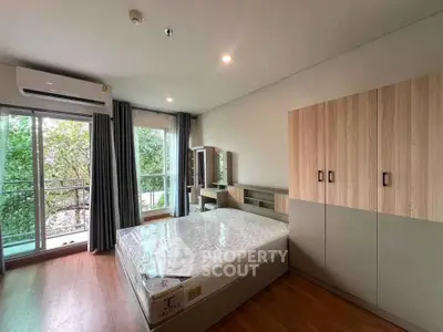 Spacious bedroom with large window and modern furnishings, offering a serene view of lush greenery.