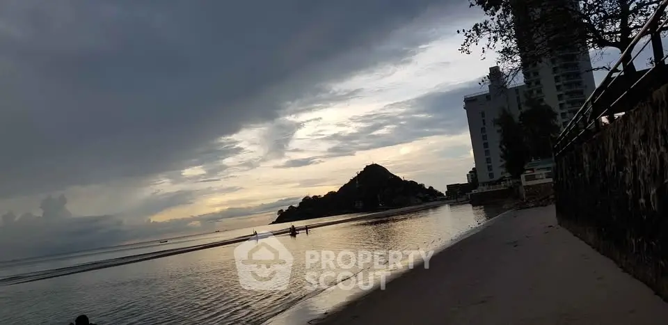 Scenic beachfront view with modern building and serene ocean at sunset.