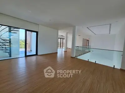 Spacious modern living area with wooden flooring and glass railing, perfect for stylish living.