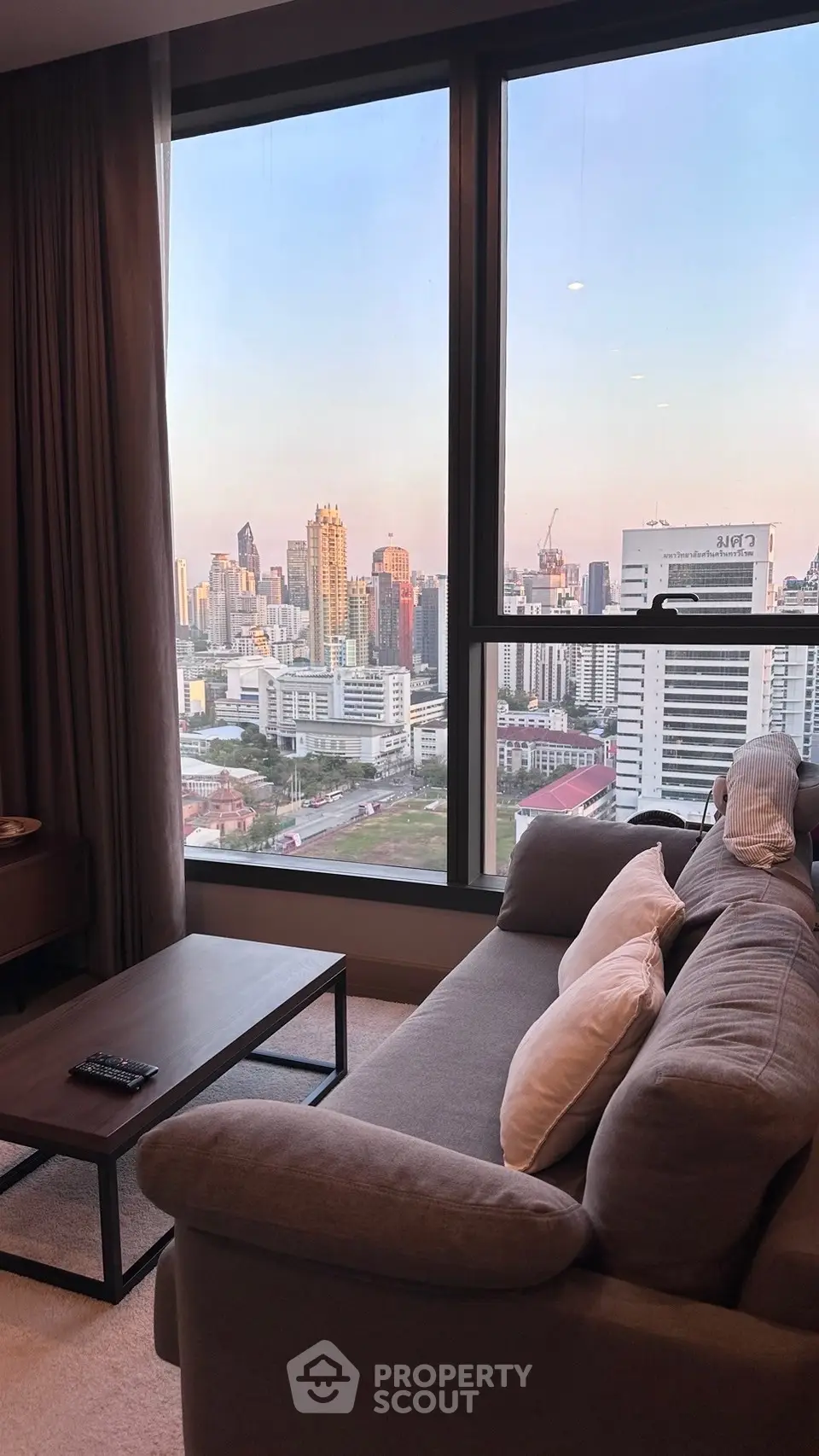 Stylish living room with panoramic city view from large windows, featuring modern sofa and coffee table.