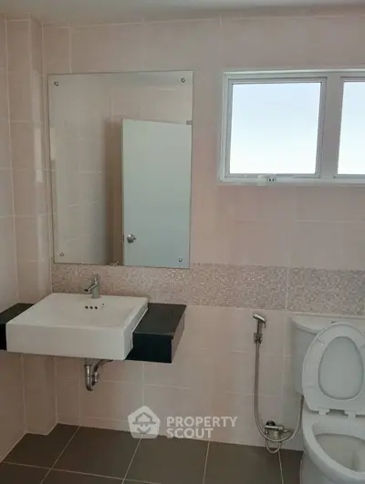 Modern bathroom with sleek sink and toilet, featuring neutral tiles and a large mirror.